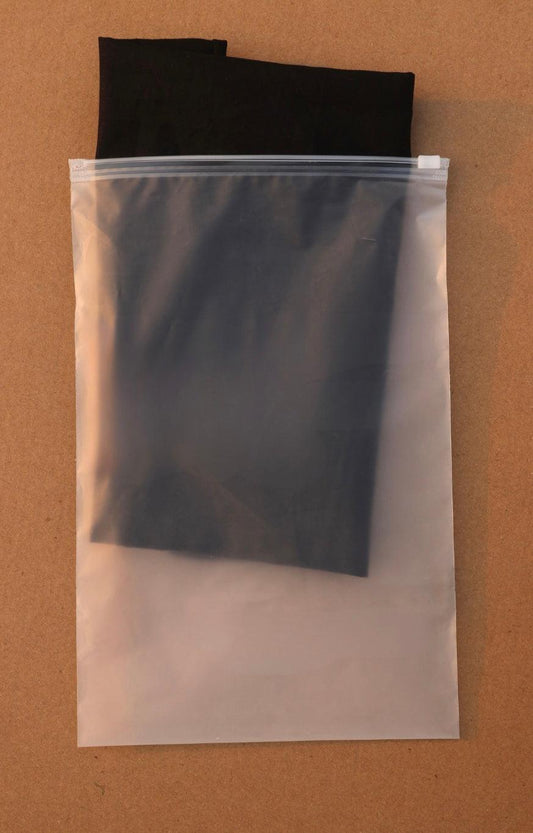 A clear plastic zip-top storage bag containing folded black fabric, placed on a brown background.