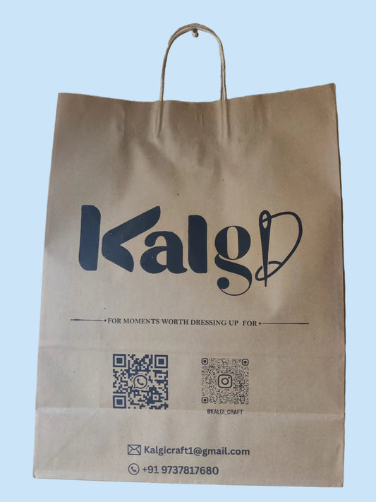 A brown kraft paper shopping bag with twisted paper handles, featuring the stylized brand name 'Kalgi' in dark blue lettering. The bag includes contact information and QR codes at the bottom, photographed hanging against a textured beige wall.